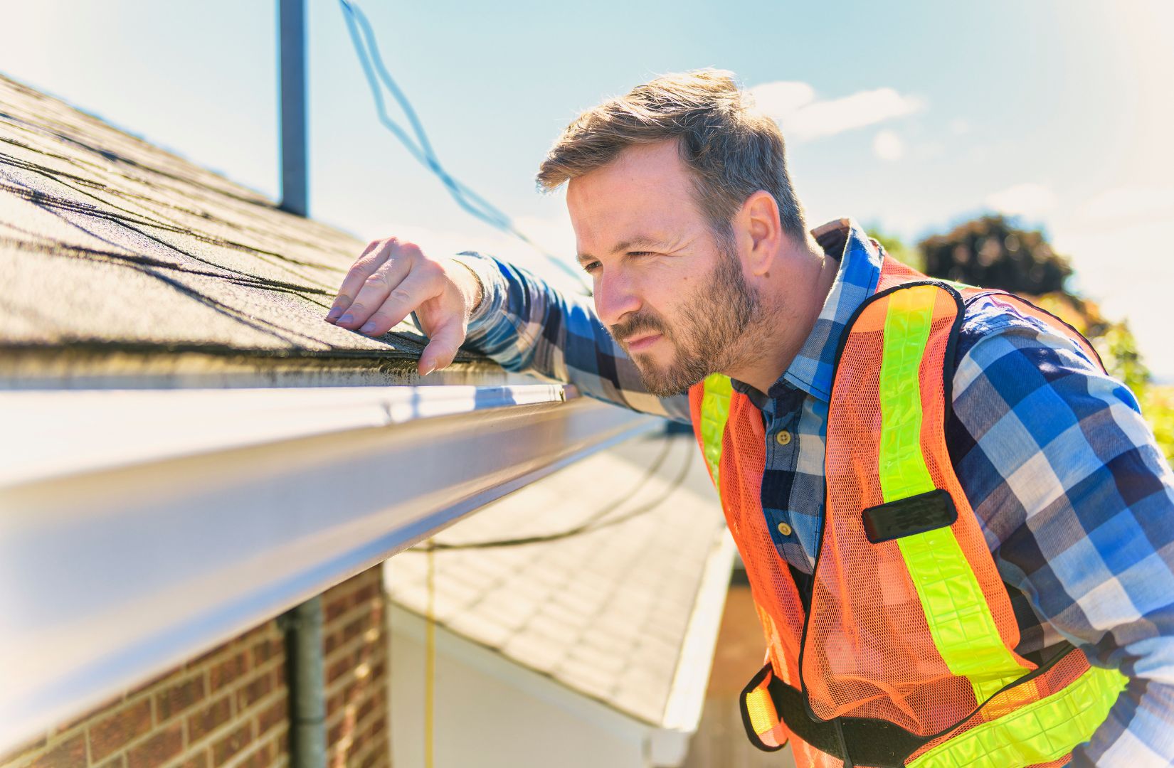 A roofing professional inspecting shingles along the roof edge